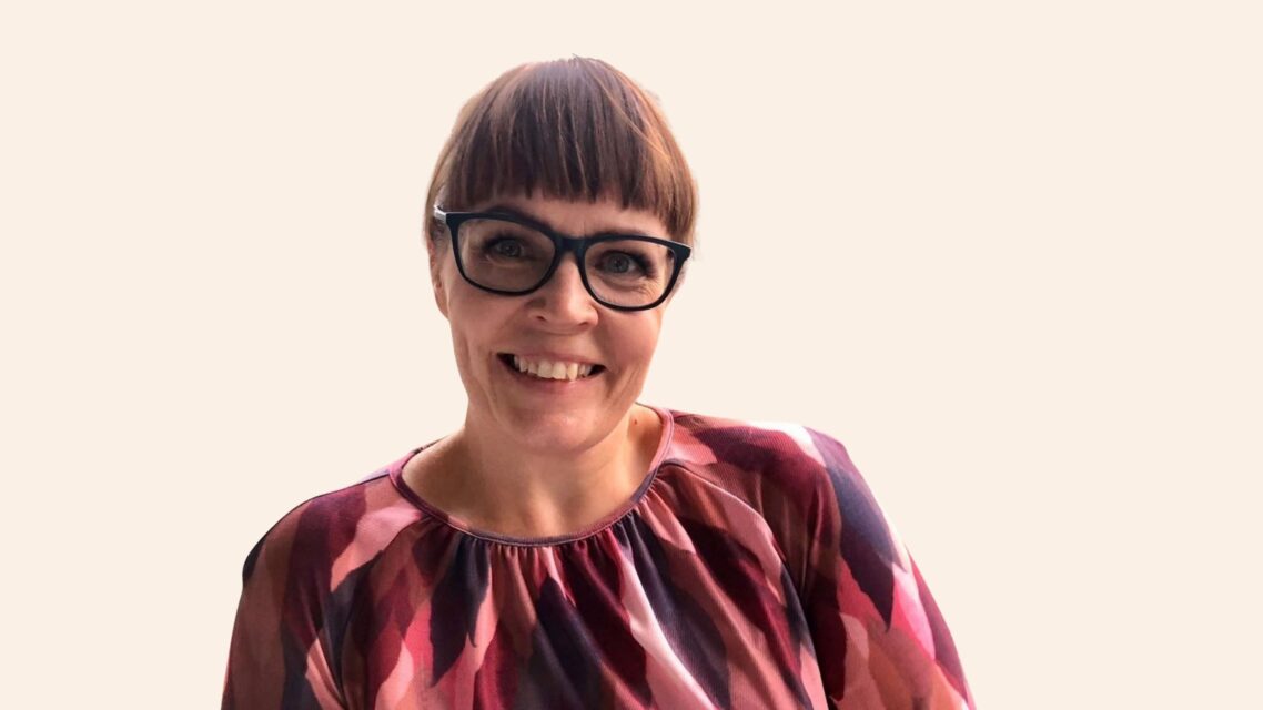 Hymyilevä Riikka Koponen katsoo kameraan. Hänellä on mustasankaiset silmälasit ja tummanruskeat hiukset.